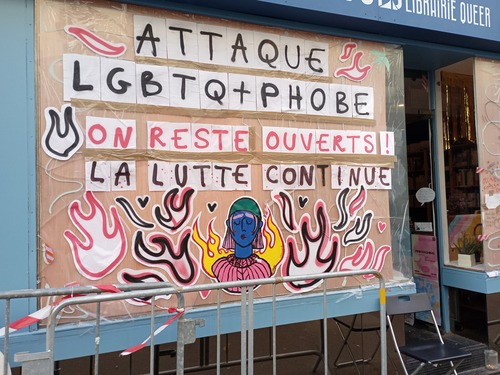 La vitrine brisée, avec dessus des dessins et en gros le message "Attaque LGBTQ+phobe. On reste ouverts ! La lutte continue"